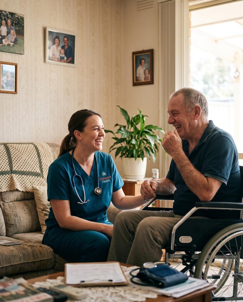 An Alabaster Health community nurse crouched at eye level beside a man who uses a wheelchair, both laughing together in his lounge room.